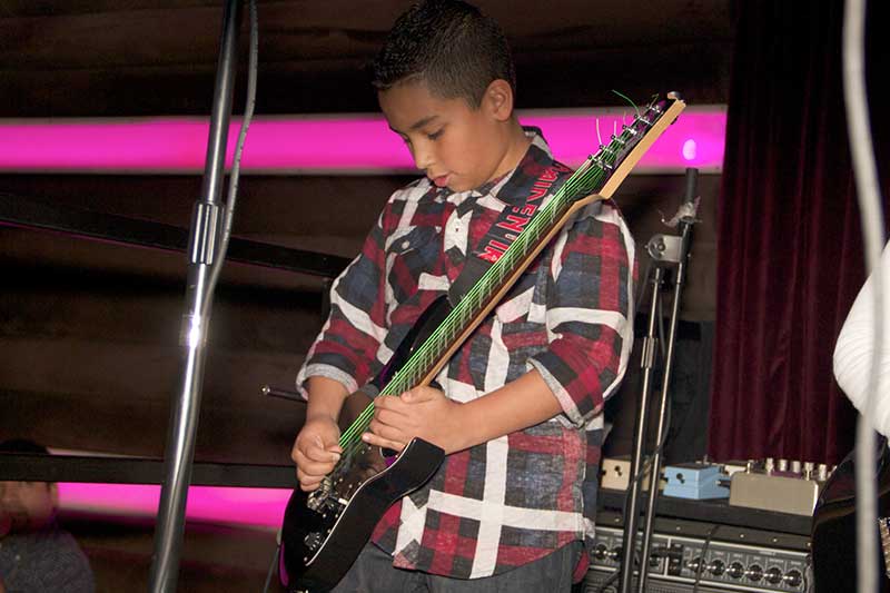Kid playing guitar on stage after guitar lessons program ended